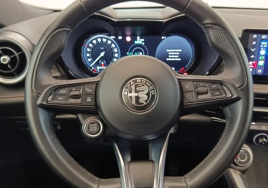 Vue rapprochée du volant en cuir noir de l'Alfa Romeo Tonale 1.5T Hybrid 160 VGT avec tableau de bord digital allumé.