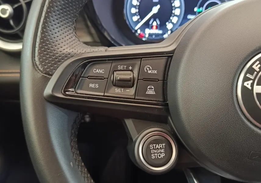 Gros plan sur le volant cuir noir de l'Alfa Romeo Tonale bleu, avec commandes de régulateur et bouton démarrage.
