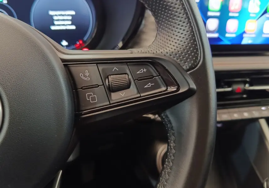 Gros plan sur les commandes gauche du volant cuir de l'Alfa Romeo Tonale 1.5T Hybrid 160 VGT, intérieur moderne.