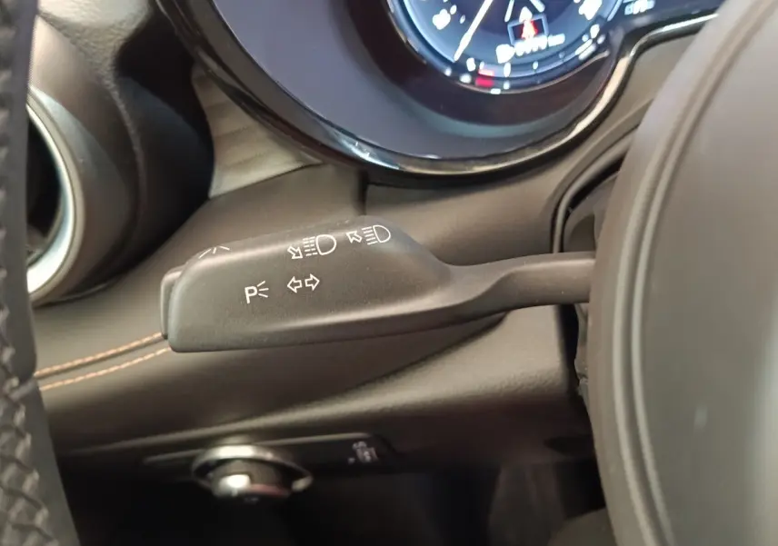 Gros plan sur la commande des clignotants et feux à gauche du volant dans l’habitacle noir de l’Alfa Romeo Tonale.