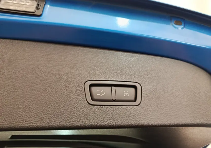 Gros plan sur la commande de fermeture électrique du coffre, entourée de la peinture bleue du hayon arrière.