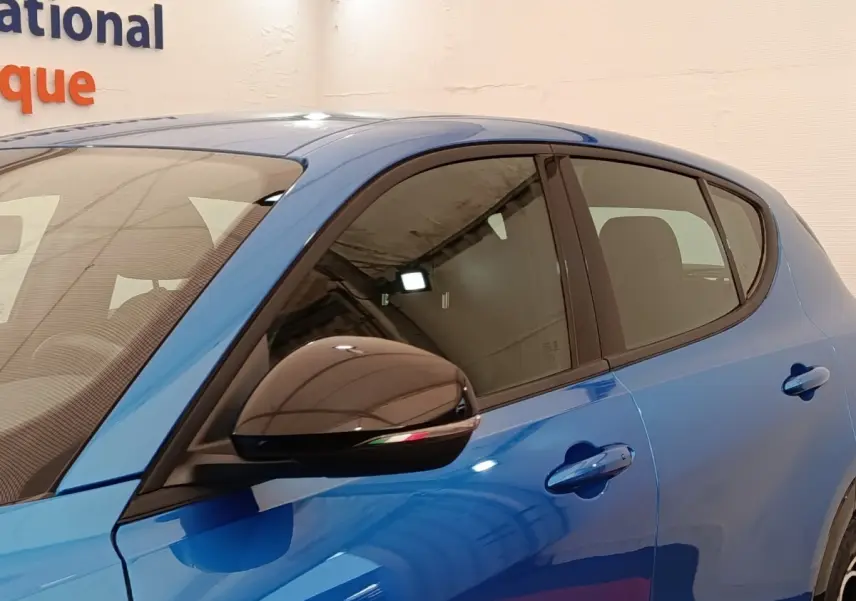 Vue latérale gauche rapprochée de l'Alfa Romeo Tonale bleu avec rétroviseur noir et poignées de porte assorties.