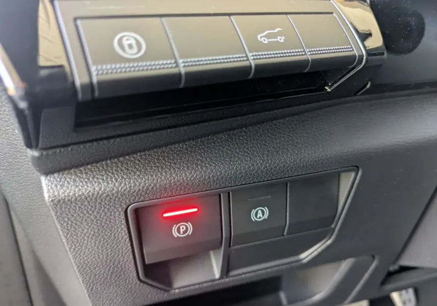 Gros plan sur les commandes électroniques du frein à main et du système start-stop dans un Renault Espace VI noir étoile.