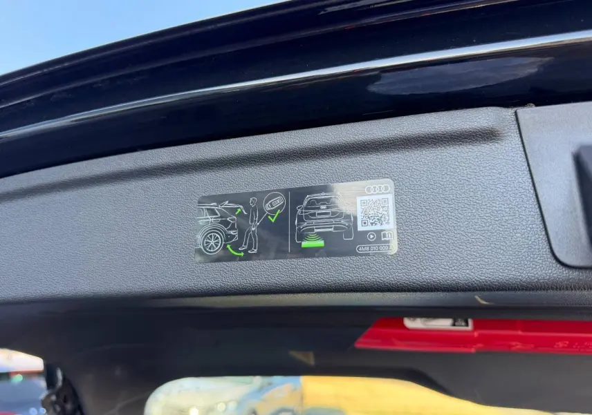 Vue rapprochée de l’intérieur du coffre ouvert d’une Audi A3 Sportback noir Mythic métallisé, avec consigne d’utilisation affichée.