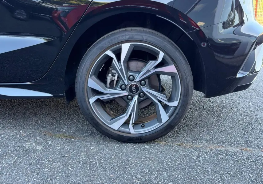 Gros plan sur la roue arrière droite d'une Audi A3 Sportback 2025 noir Mythic métallisé avec jante alu design S line.