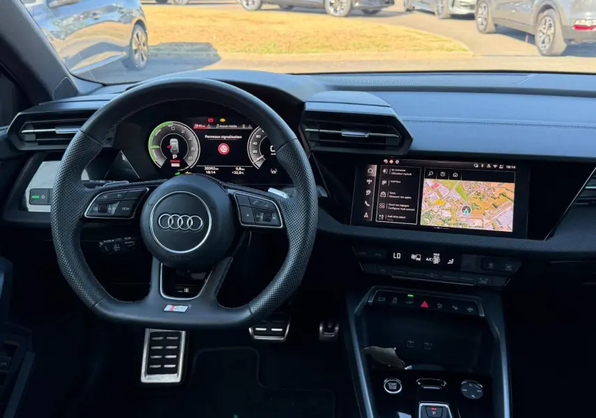 Vue intérieure frontale du tableau de bord noir de l'Audi A3 Sportback 2025 avec volant sport et écran multifonction.