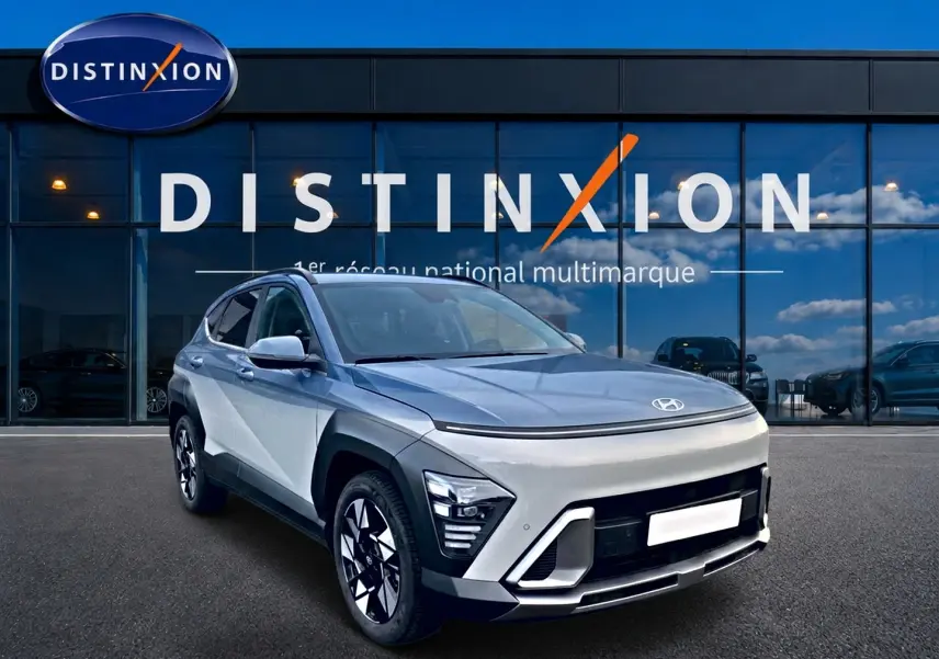 Vue 3/4 avant droit d'un Hyundai Kona gris clair avec jantes alliage et calandre au design futuriste devant un showroom Distinxion.
