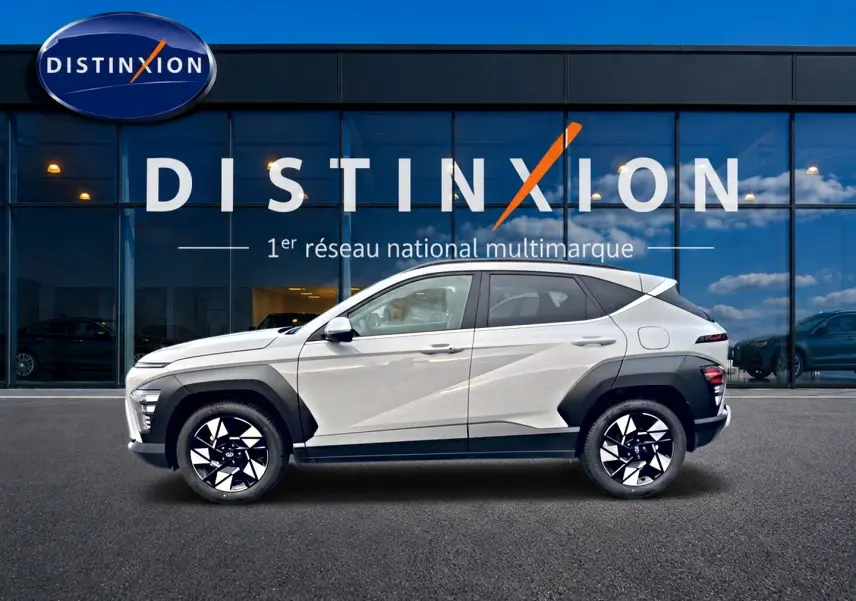 Vue latérale droite d'un Hyundai Kona gris 2025 avec protections noires et jantes alliage bicolores devant une vitrine Distinxion.