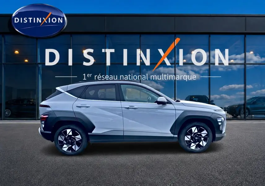 Profil côté gauche d'un Hyundai Kona gris 2025 avec protections noires et jantes alliage bicolores devant un showroom Distinxion.