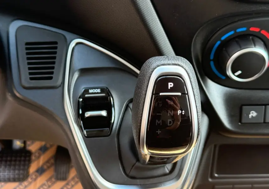 Gros plan sur le levier de vitesses automatique noir et chrome de l'IVECO Daily blanc, avec commandes de climatisation en arrière-plan.