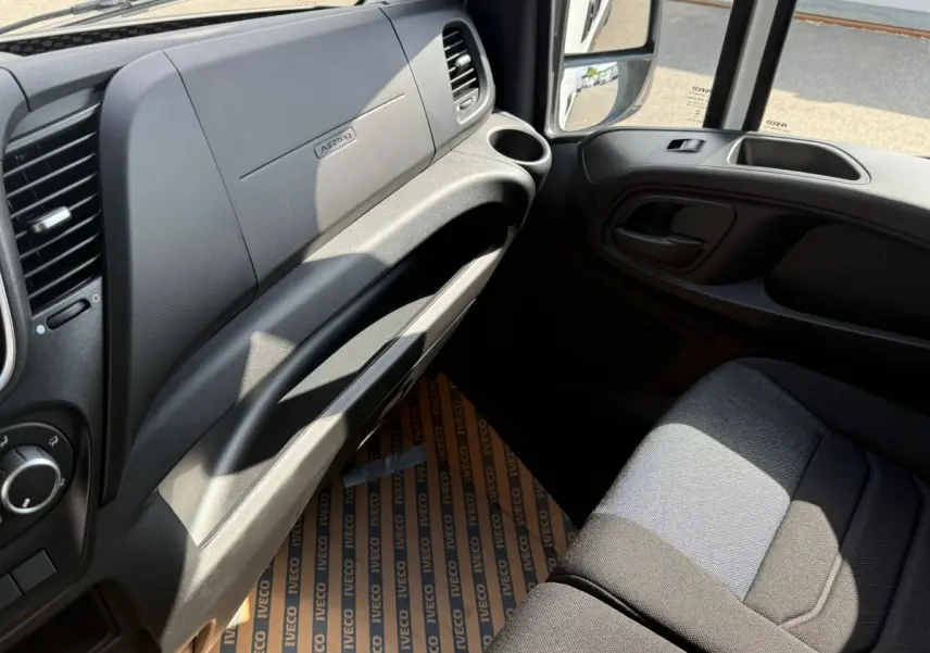 Vue intérieure côté passager du tableau de bord et siège gris foncé du fourgon Iveco Daily blanc, avec porte ouverte.