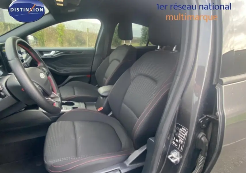 Vue intérieure côté conducteur de la Ford Focus gris foncé 2024, sièges noirs avec surpiqûres rouges et accoudoir central.