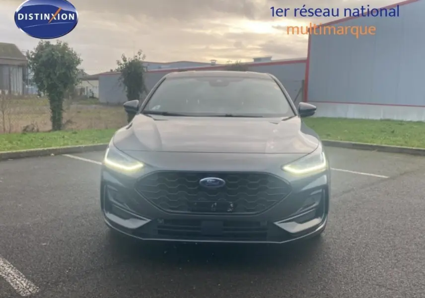 Vue avant d'une Ford Focus 1.5 EcoBlue gris foncé avec phares LED allumés sur parking extérieur.