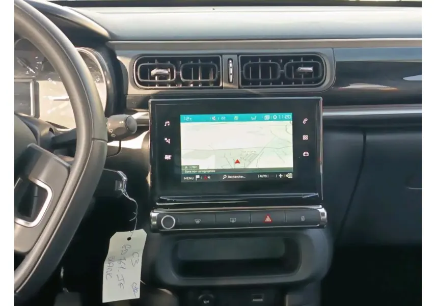 Vue intérieure centrée sur la console centrale noire avec écran GPS tactile et volant partiel d'une Citroën C3 blanche.