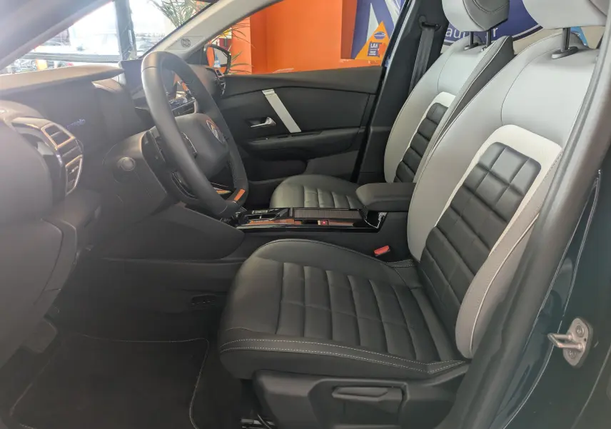 Vue intérieure côté conducteur de la Citroën C4 hybride 2025, sièges bi-ton gris et noir avec console centrale noire brillante.