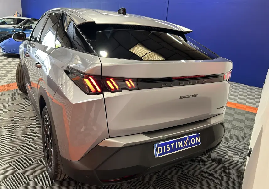 Vue 3/4 arrière droite du Peugeot 3008 gris Artense avec feux arrière LED et toit noir brillant en intérieur showroom.