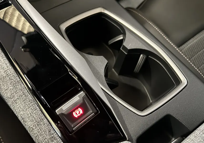 Gros plan intérieur sur la console centrale noire et grise avec porte-gobelets et bouton frein à main électrique rouge du Peugeot 3008 gris Artense.