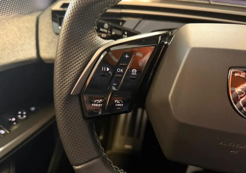 Gros plan sur les commandes gauche du volant perforé du Peugeot 5008 Hybrid 145 e-DCS6 GT, intérieur noir.