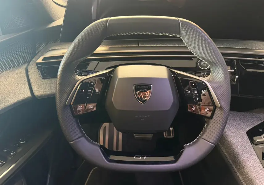 Vue rapprochée du volant GT du Peugeot 5008 Hybrid 145, avec commandes intégrées et surpiqûres blanches.