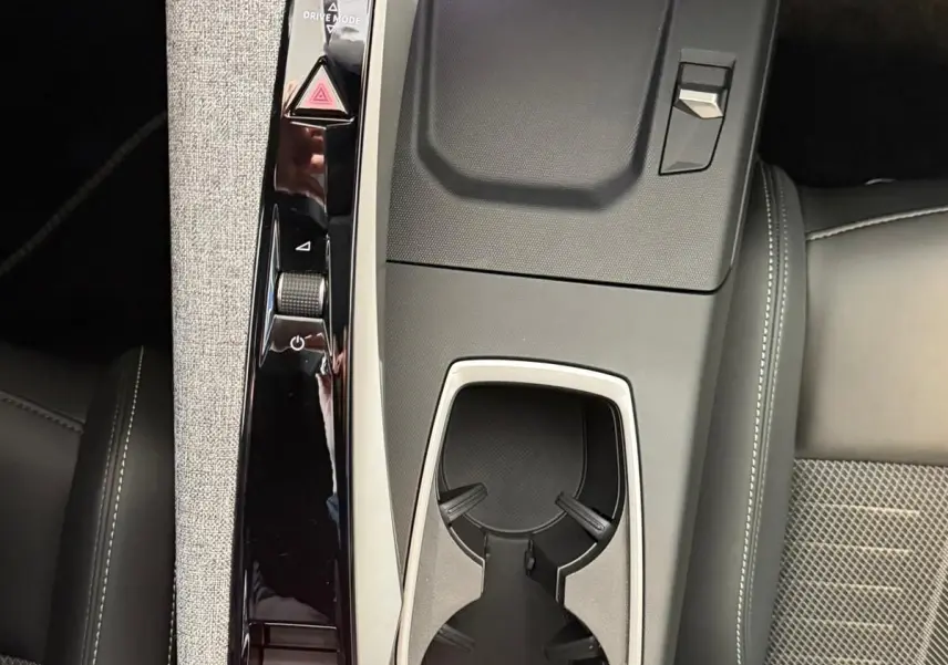 Vue plongeante sur la console centrale du Peugeot 5008 Hybrid 145 GT, avec accoudoir tissu gris et porte-gobelets noirs.