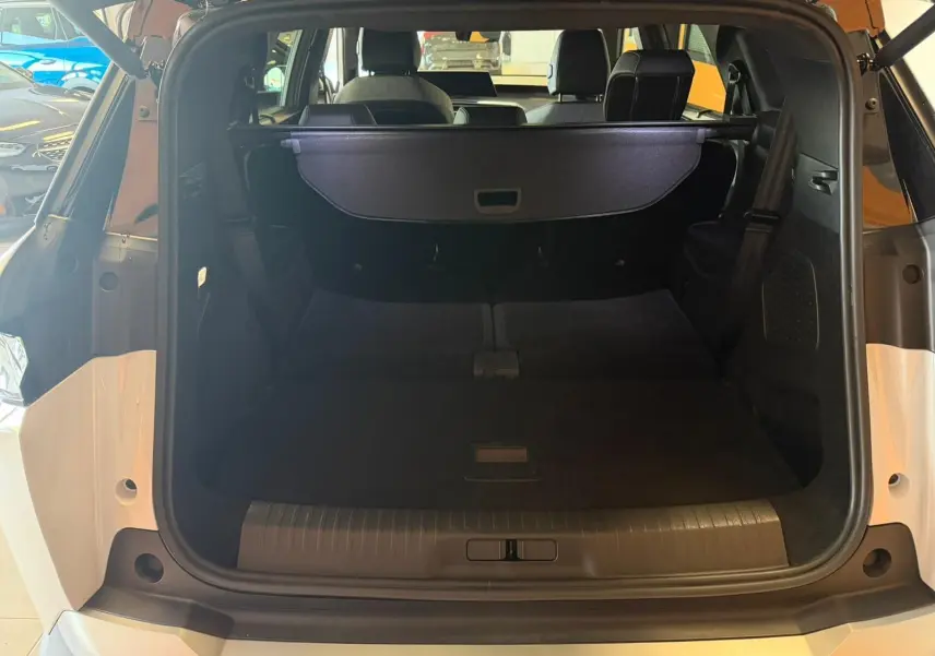 Vue arrière ouverte du coffre du Peugeot 5008 Hybrid 145 e-DCS6 GT blanc Okenite avec toit noir, montrant l'espace de chargement.