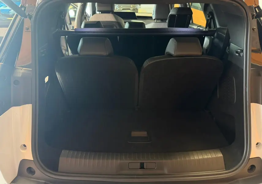 Vue arrière du coffre ouvert du Peugeot 5008 Hybrid blanc Okenite, montrant les sièges arrière et l'espace de chargement.