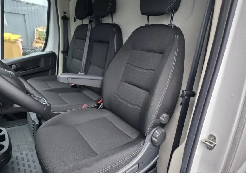 Vue intérieure côté conducteur du Peugeot Boxer Fourgon 2025, sièges tissu noir avec accoudoir et ceintures visibles.