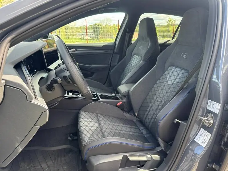 Intérieur avant de la Volkswagen Golf 1.5 eTSI R-Line 2026 en gris lunaire, sièges sport en tissu anthracite avec surpiqûres bleues.