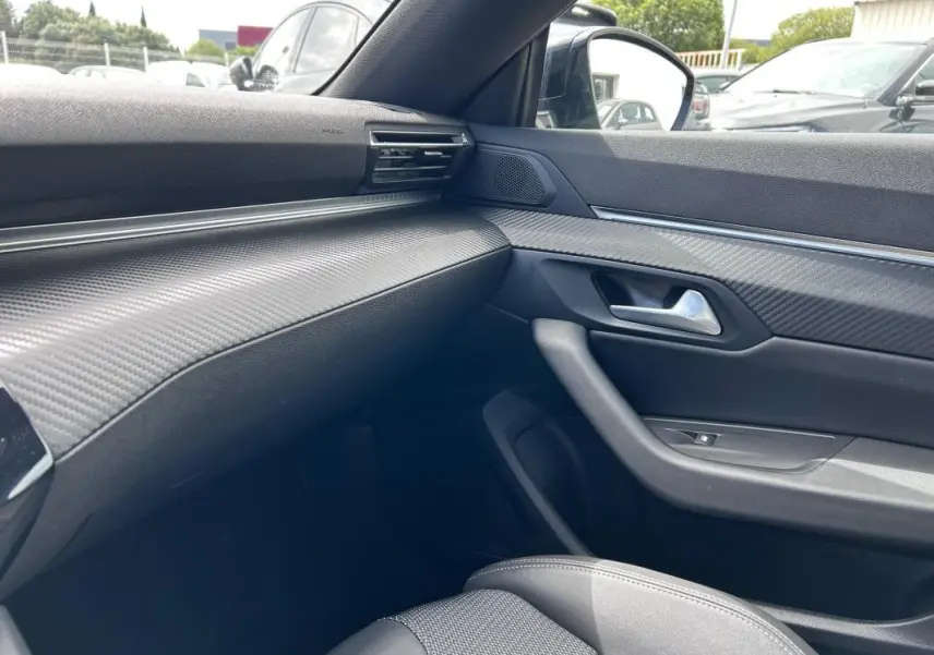 Intérieur côté passager du Peugeot 508 Hybrid 225 e-EAT8 Allure 2024, avec tableau de bord noir texturé et porte en carbone.