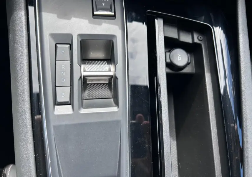 Gros plan sur la console centrale noire de la Peugeot 508 Hybrid 225 e-EAT8 avec sélecteur de boîte auto et prise 12V.