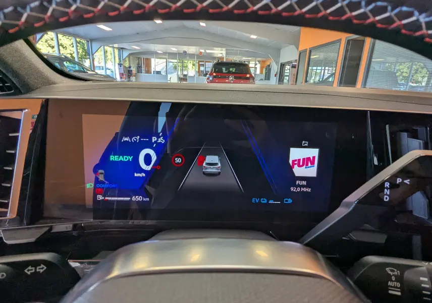 Vue intérieure du tableau de bord numérique du Renault Espace VI hybride, affichant la vitesse, la radio et l'assistance au stationnement.