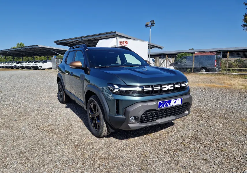 Dacia Duster 1.8 Hybrid 155 Extreme vert cèdre vu en 3/4 avant droit sur un sol gravillonné, avec rétroviseurs bronze.