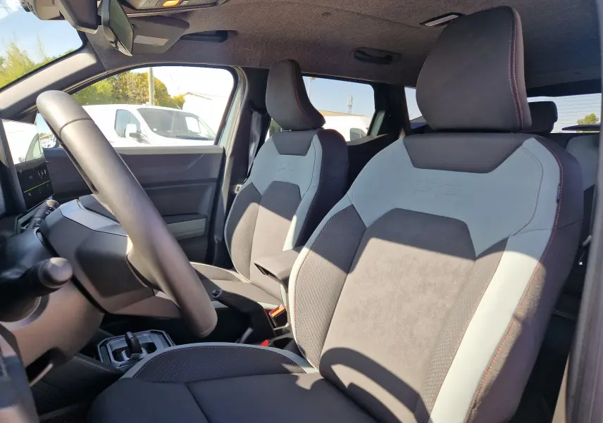 Vue intérieure côté avant gauche du Dacia Duster 1.8 Hybrid 155 avec sièges bi-ton gris et noir au design marqué.