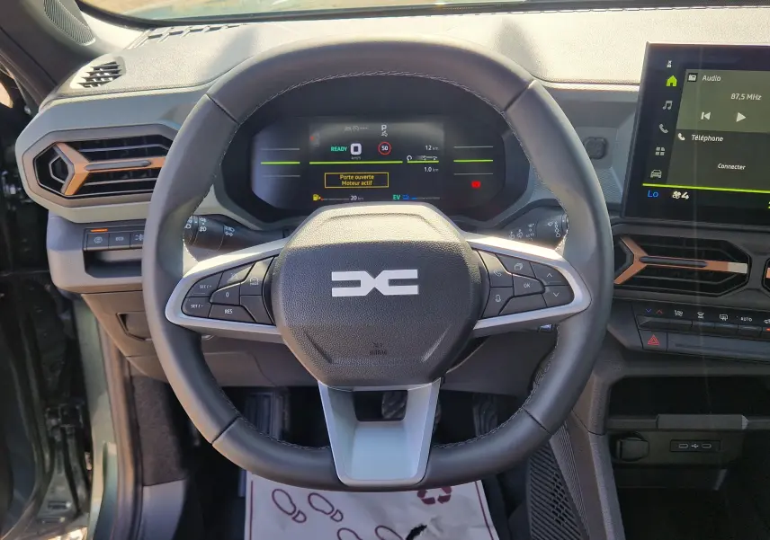 Vue intérieure centrée sur le volant du Dacia Duster 1.8 Hybrid 155, avec tableau de bord numérique et touches multifonctions.