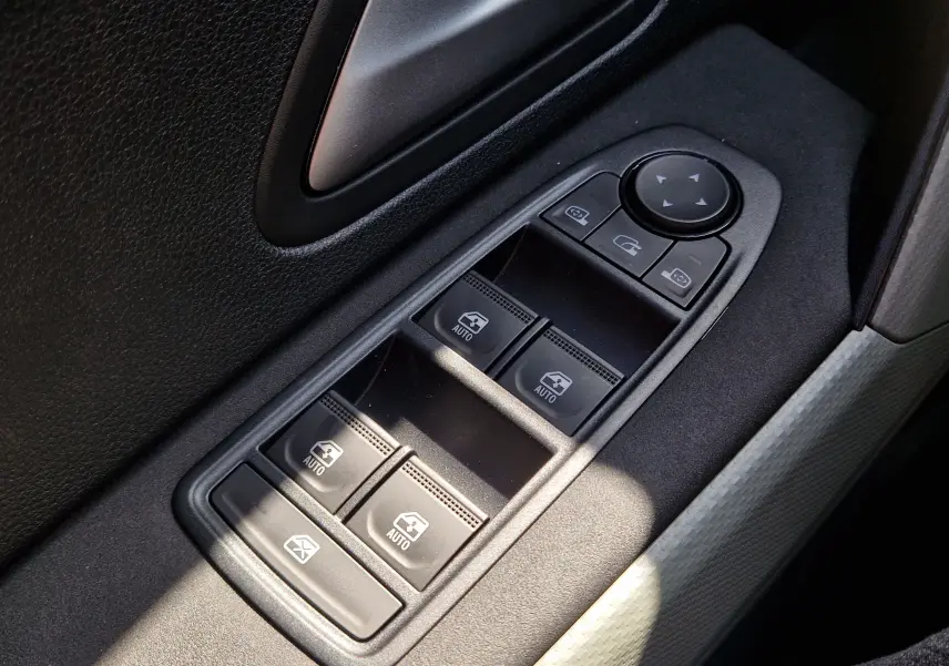 Gros plan sur les commandes des vitres électriques et rétroviseurs côté conducteur du Dacia Duster 1.8 Hybrid 155, intérieur noir.