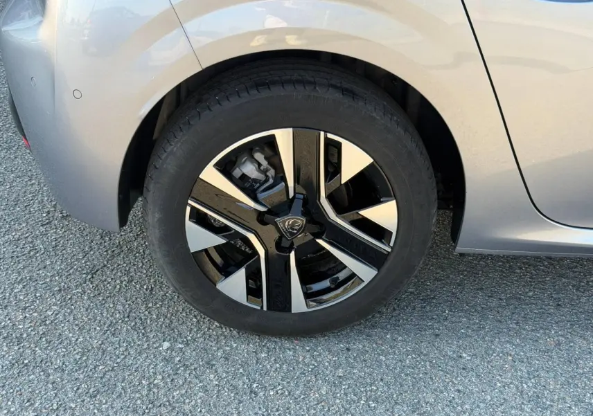 Gros plan sur la roue avant gauche d'une Peugeot 208 gris Artense avec jante alu bicolore moderne.