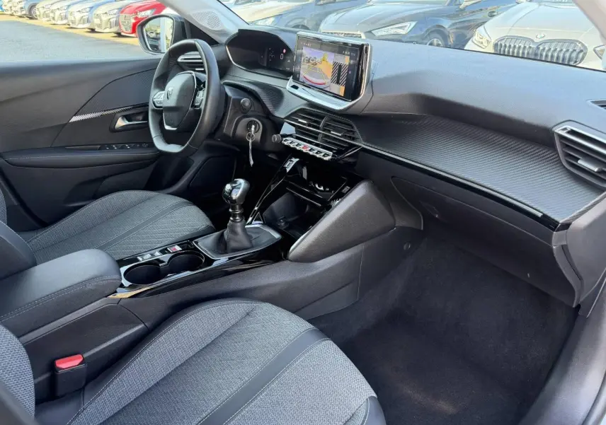 Vue intérieure côté conducteur de la Peugeot 208 1.2 100ch 2025, montrant la console centrale avec boîte manuelle et écran tactile.