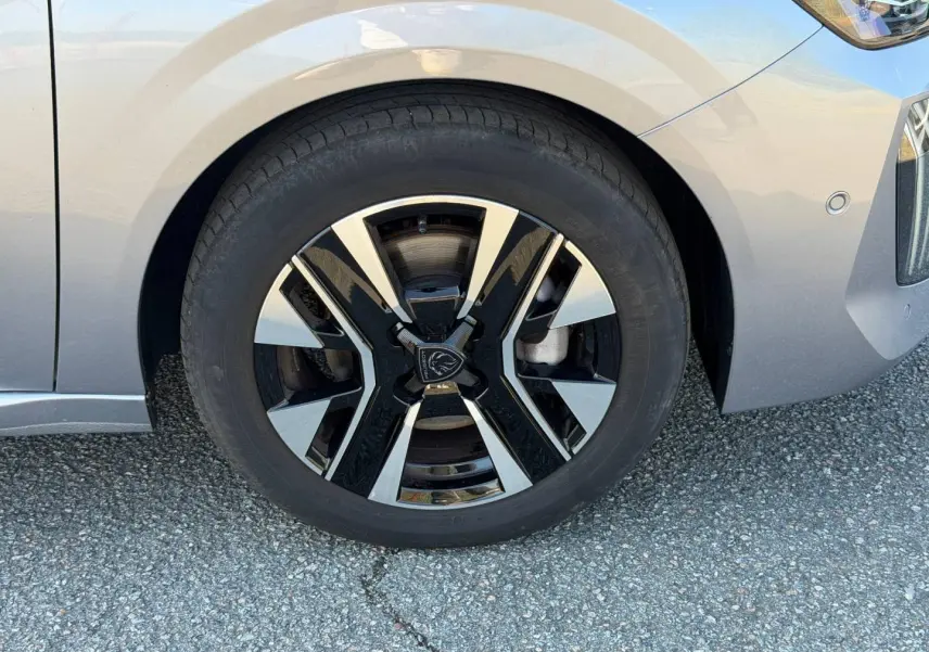 Gros plan sur la roue avant gauche d'une Peugeot 208 gris Artense avec jante alliage bicolore moderne.
