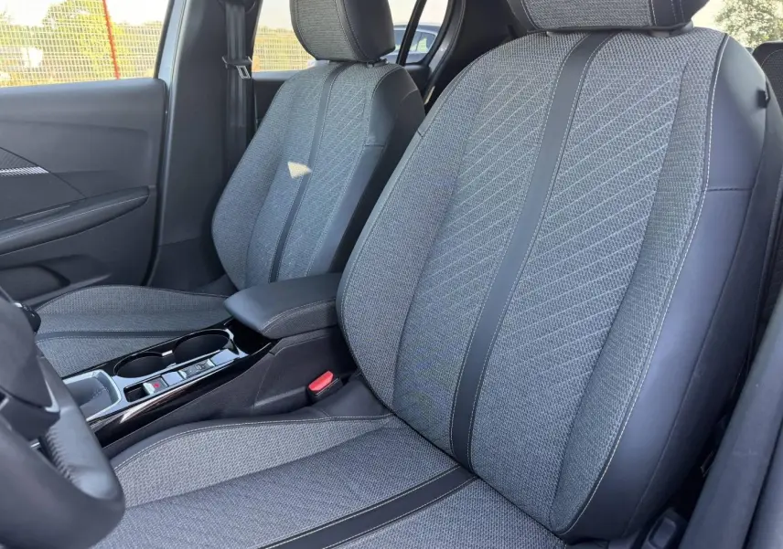 Vue intérieure côté conducteur de la Peugeot 208 1.2 100ch gris Artense, sièges tissu gris avec surpiqûres noires.