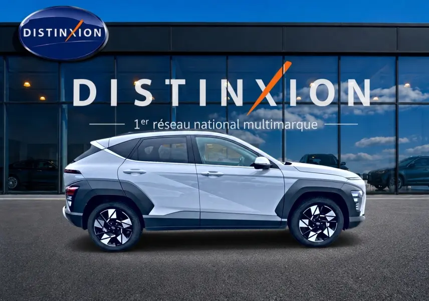 Vue latérale droite d'un Hyundai Kona gris 2025 avec protections noires et jantes alliage bicolores devant une vitrine Distinxion.