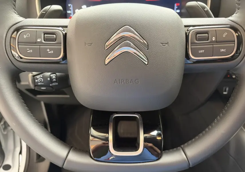 Gros plan sur le volant cuir noir du Citroën C5 Aircross 2025 avec commandes multifonctions et logo chromé central.