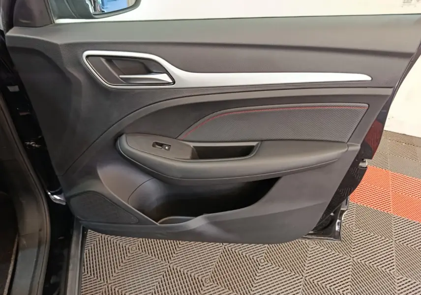Gros plan sur la porte intérieure côté gauche noire du MG Motor ZS Luxury 2024 avec surpiqûres rouges et poignée chromée.