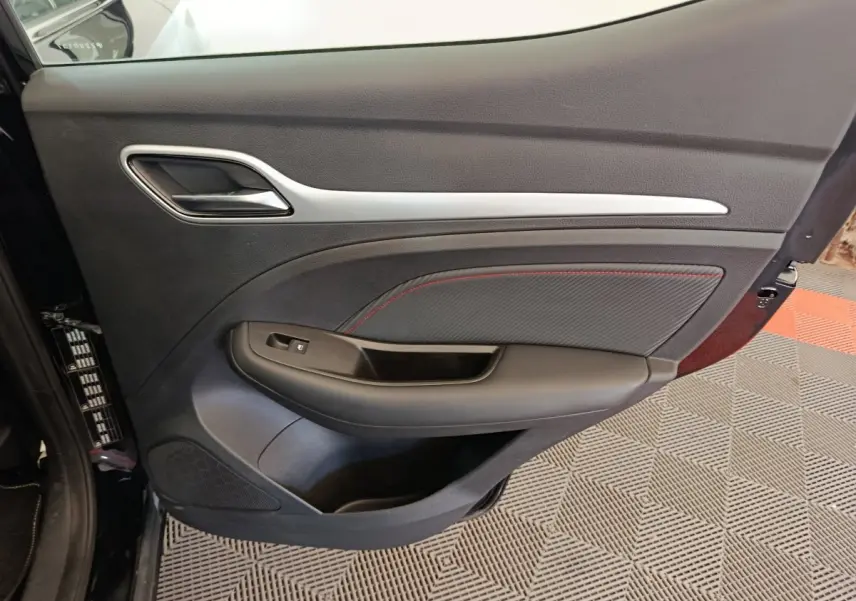 Vue côté intérieur de la porte avant gauche du MG ZS Luxury noir, avec surpiqûres rouges et poignée chromée.