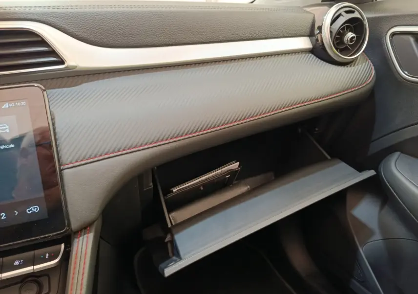 Intérieur côté passager du MG ZS Luxury 2024, tableau de bord gris avec surpiqûres rouges et boîte à gants ouverte.