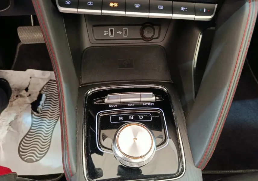 Vue rapprochée de la console centrale noire du MG ZS Luxury 70kWh 2024 avec molette de sélection de vitesse et surpiqûres rouges.