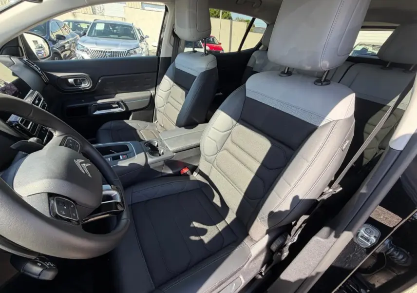 Vue intérieure côté conducteur du Citroën C5 Aircross hybride 2024 noir, avec sièges bi-ton gris et noir et volant multifonction.