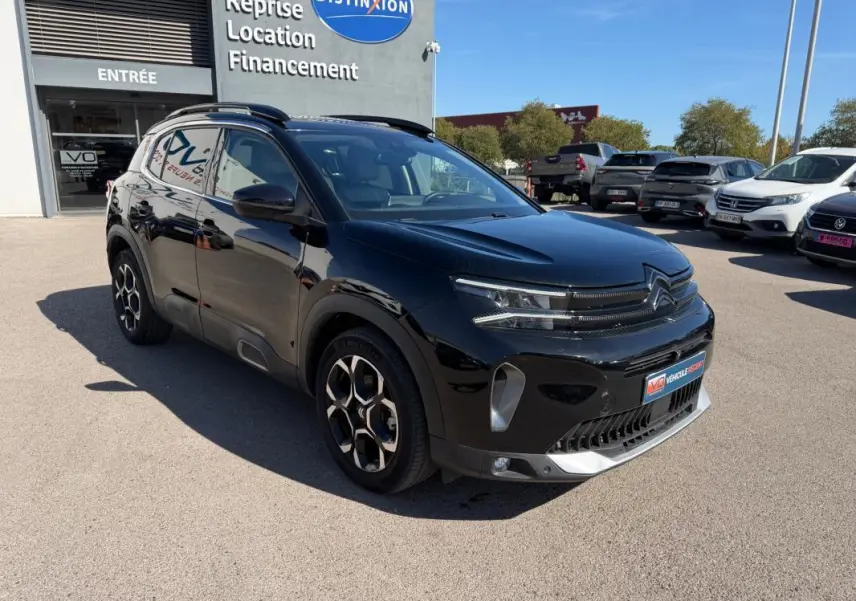 Citroën C5 Aircross Hybride noir vue 3/4 avant droit, avec jantes distinctives et calandre moderne, stationné devant un concessionnaire.