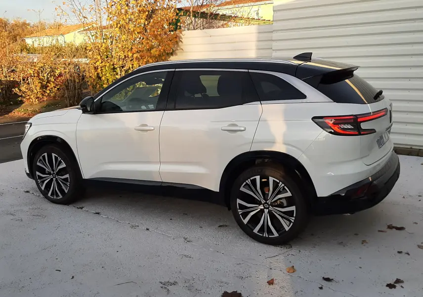 Vue latérale droite d'un Renault Austral 2025 blanc nacré avec toit noir et jantes alliage bicolores, stationné en extérieur.