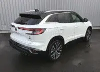 Vue 3/4 arrière droite d'un Renault Austral 2025 blanc nacré avec toit noir et jantes alliage, stationné sur sol mouillé.