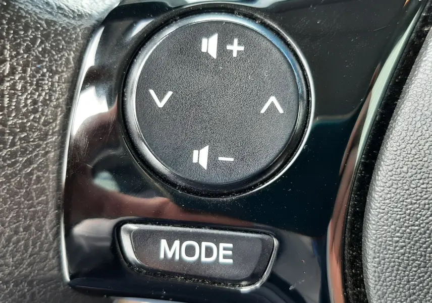 Gros plan sur les commandes de volume et mode au volant d'une Citroën C1 blanche, version 2021, intérieur noir.
